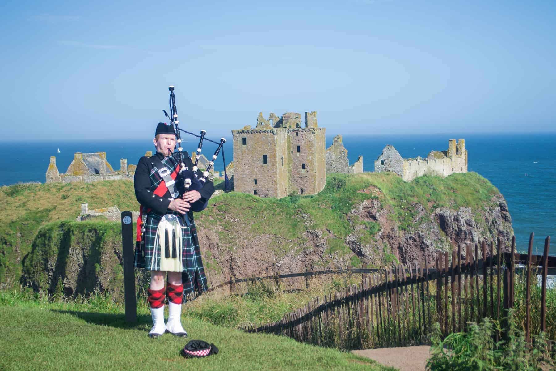 Scottish Piper at Dunnottar Castle, Aberdeenshire, Scotland. He plays pipe with the castle in background