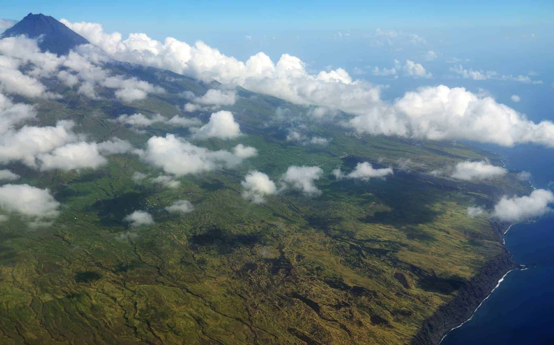 The island of Fogo, in Cabo Verde c0vered by white puffy clouds, as seen from aerial view on departure