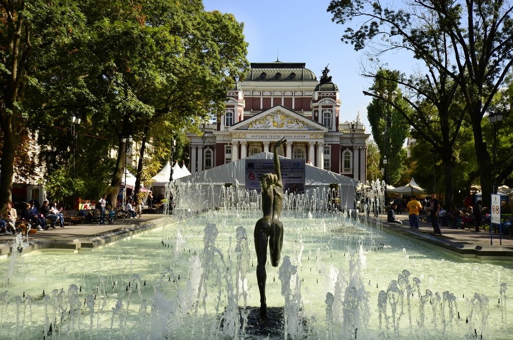 Sofia, Bulgaria: Unidentified people relaxing around the pool with small fountains and female sculpture in front of the National Theater Iwan Vazov