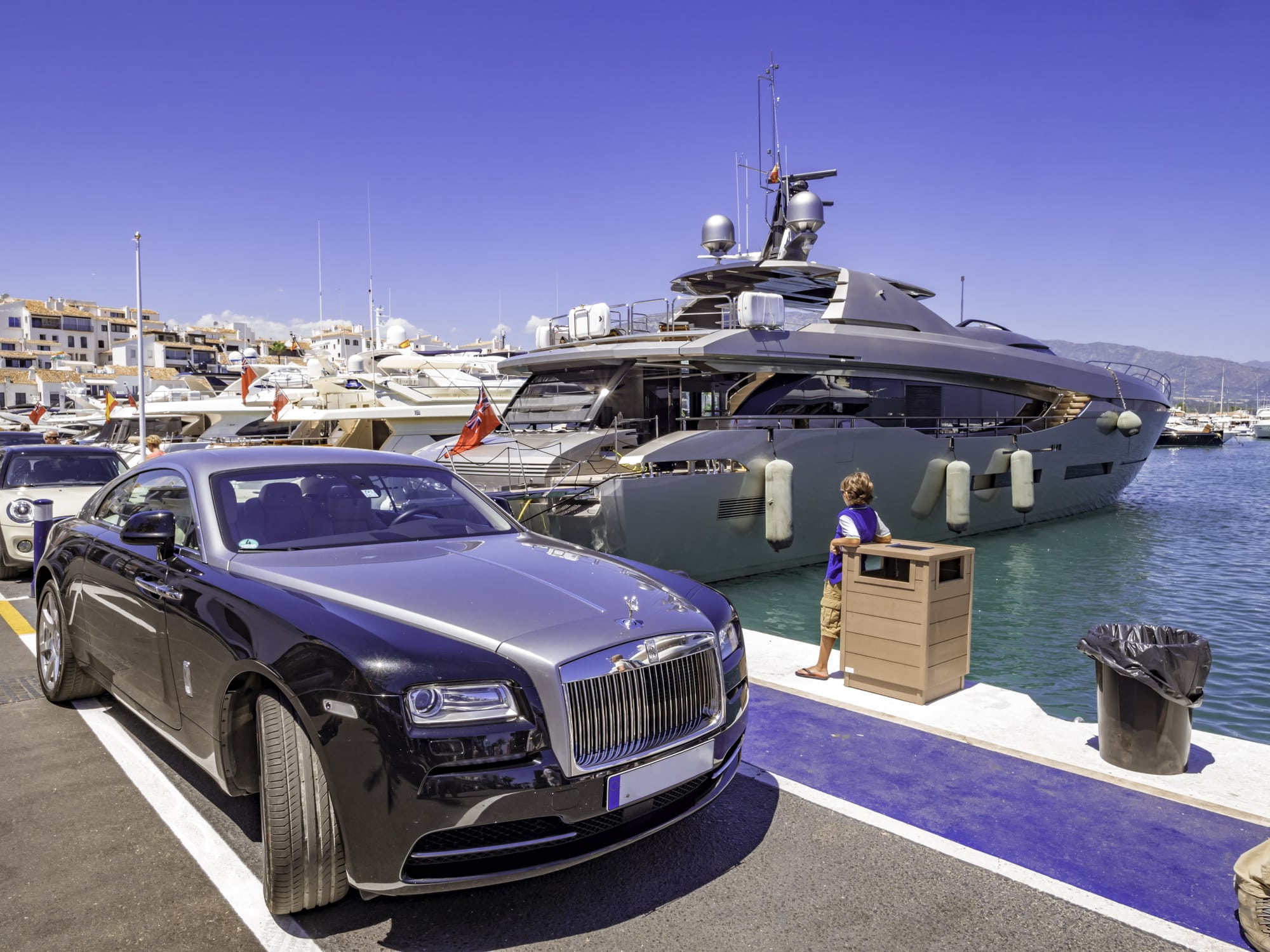 Rolls-Royce car next to a huge yacht in Puerto Banus, Marbella, a luxury harbour and marina in Marbella popular for the jetset
